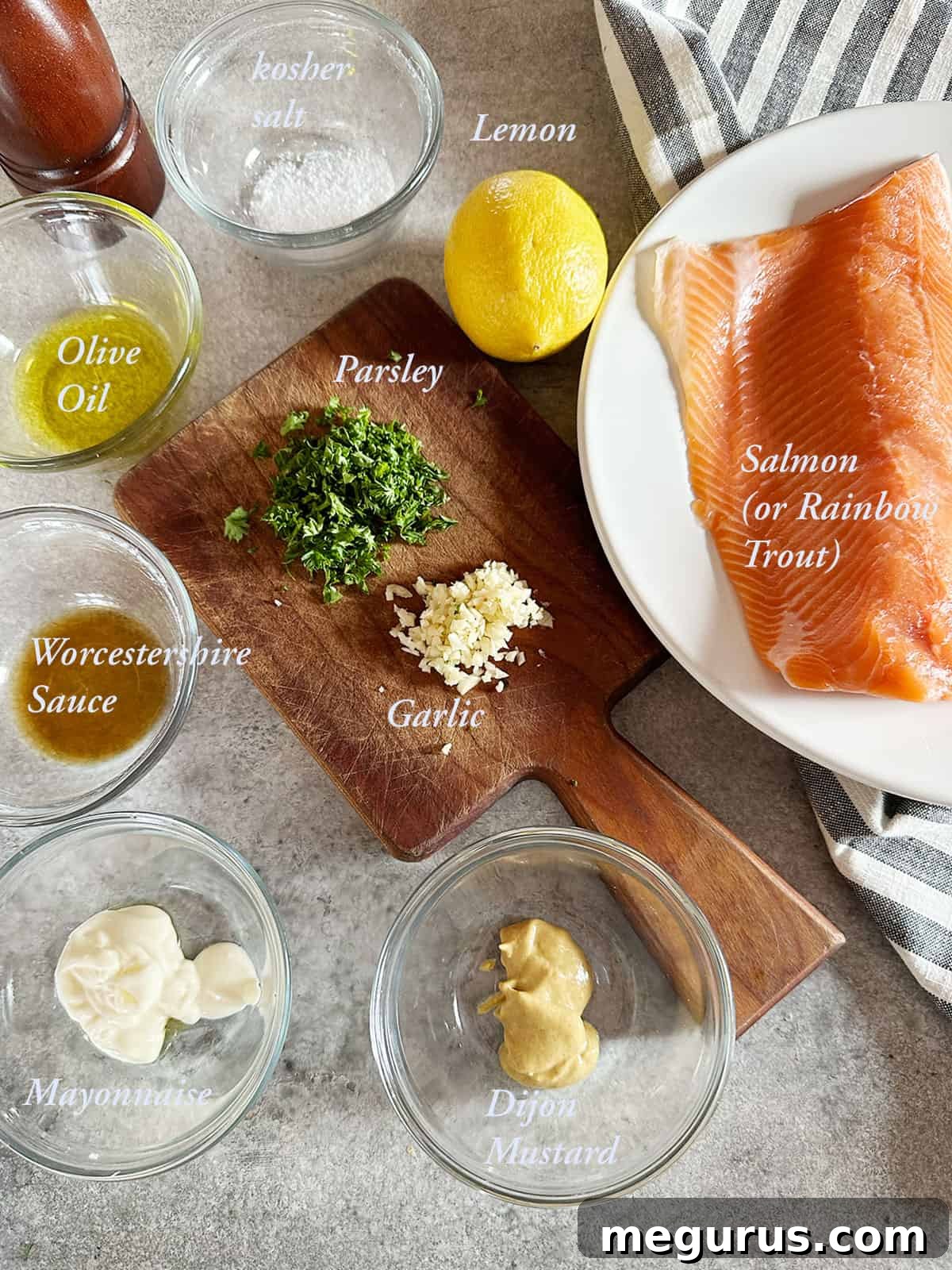 A collection of fresh ingredients laid out, including salmon fillets, Dijon mustard, mayonnaise, garlic, Worcestershire sauce, and fresh parsley, all ready to be combined for the salmon topping.
