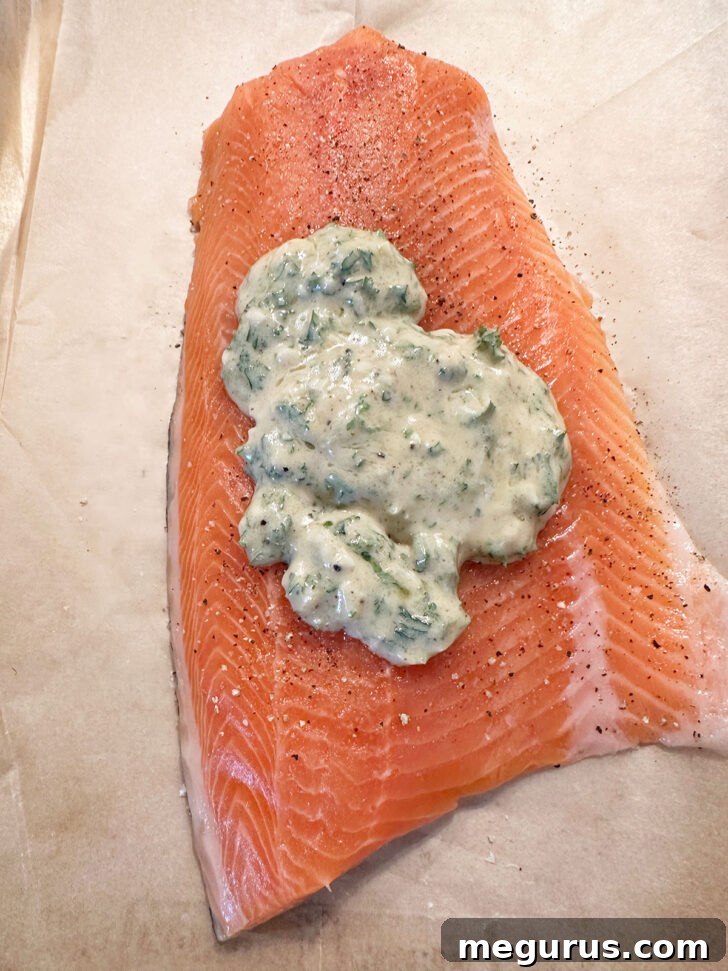 The mixed Dijon garlic topping is spooned generously over the seasoned salmon fillet on the baking sheet.