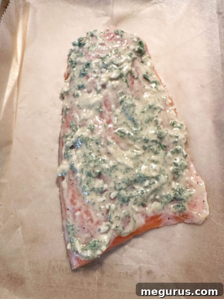 The Dijon garlic topping is evenly spread over the top and exposed sides of the salmon fillet using the back of a spoon.