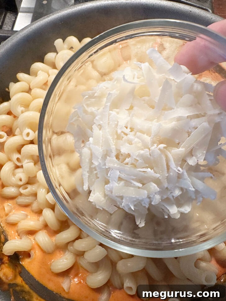 Adding grated Parmesan cheese to the pasta and sauce in the skillet.
