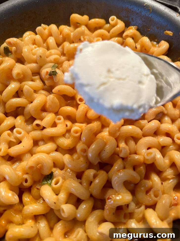 Adding dollops of seasoned ricotta cheese on top of the pasta.