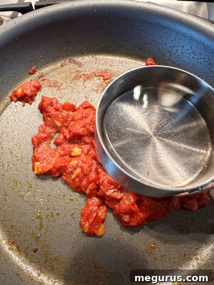 Pouring vodka into the skillet with tomato paste and aromatics.