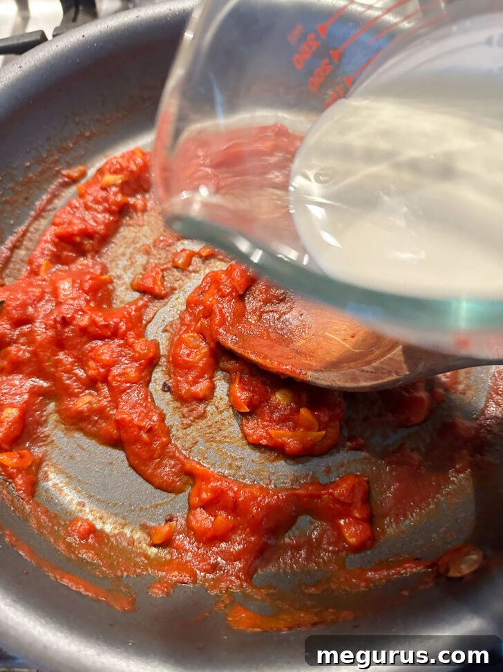 Adding heavy cream to the simmering tomato sauce in the skillet.