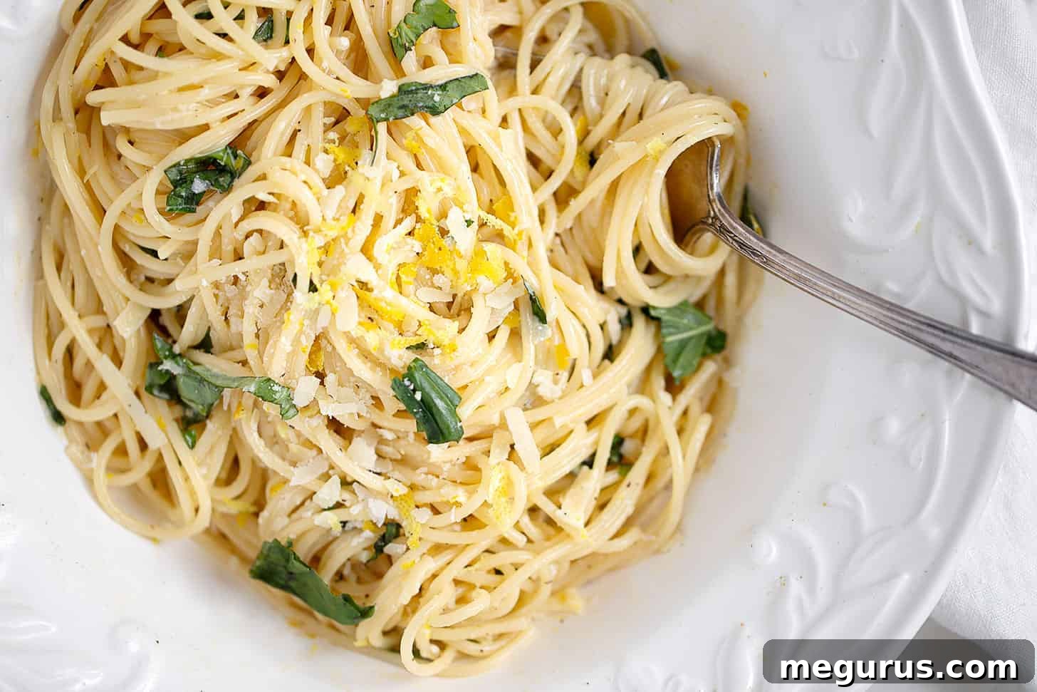 A close-up shot of creamy lemon pasta served in an elegant white bowl, garnished with fresh basil and lemon zest.