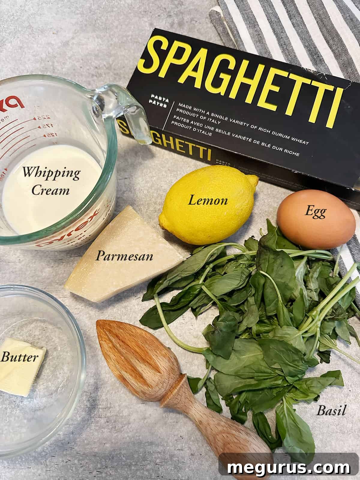 A flat lay of fresh ingredients laid out for making creamy lemon pasta, including lemons, heavy cream, egg, basil, and Parmesan cheese.