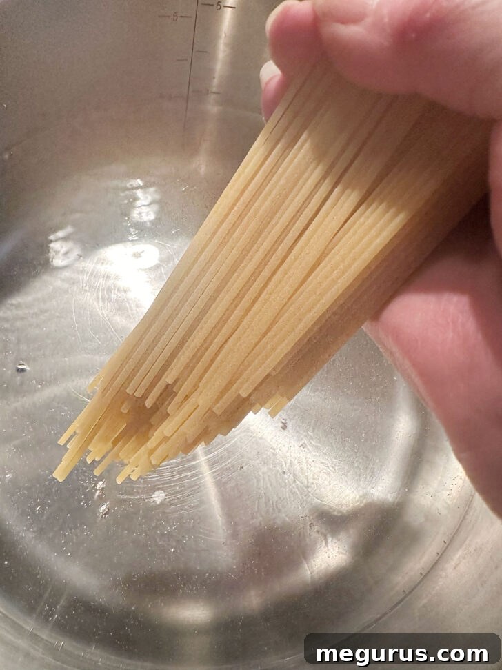 Dried spaghetti being added to a large pot of vigorously boiling, salted water, ready for cooking.