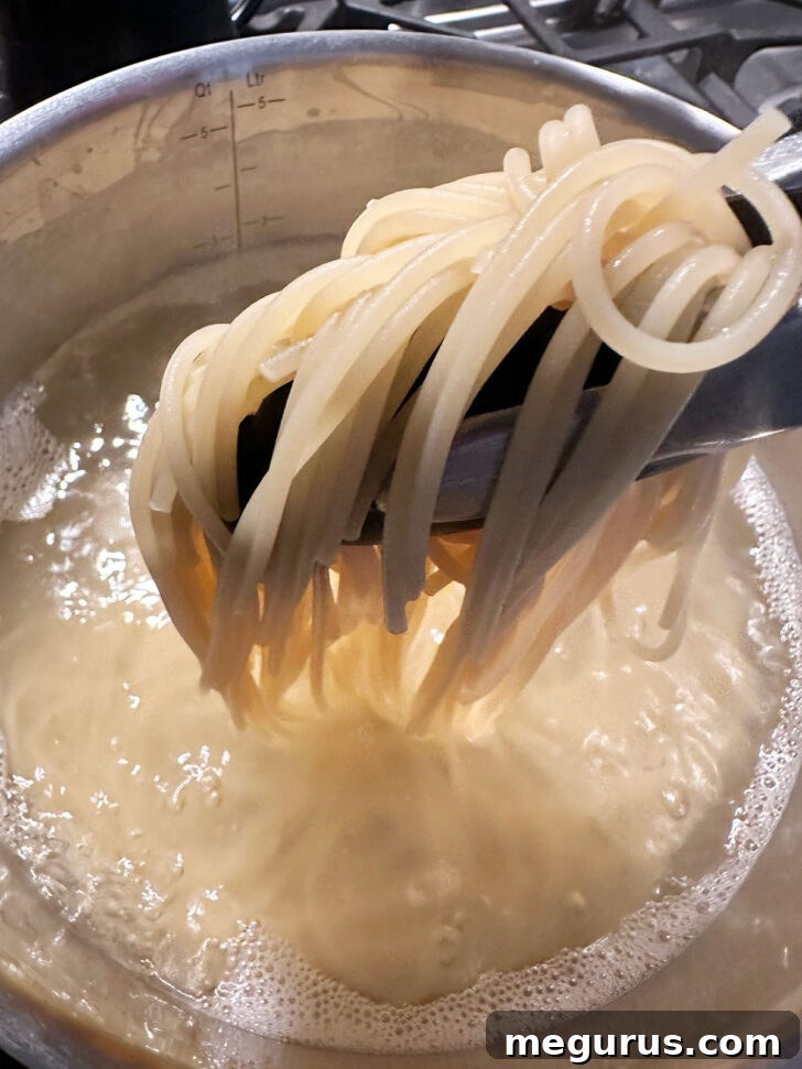 Cooked spaghetti being carefully lifted from the boiling water with tongs, allowing excess water to drip back into the pot.