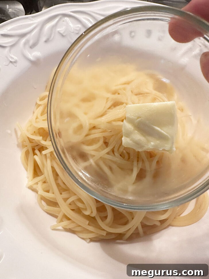 A knob of butter being added to the hot, freshly cooked pasta in a bowl, ready to be tossed.