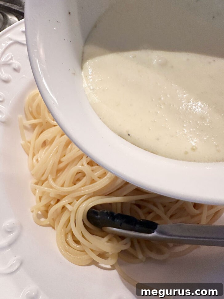 The prepared lemon cream sauce being poured generously over the hot, buttered pasta in the serving bowl.