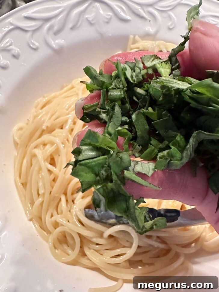 Fresh basil leaves being added to the creamy lemon pasta in the bowl, ready for a final toss and serving.
