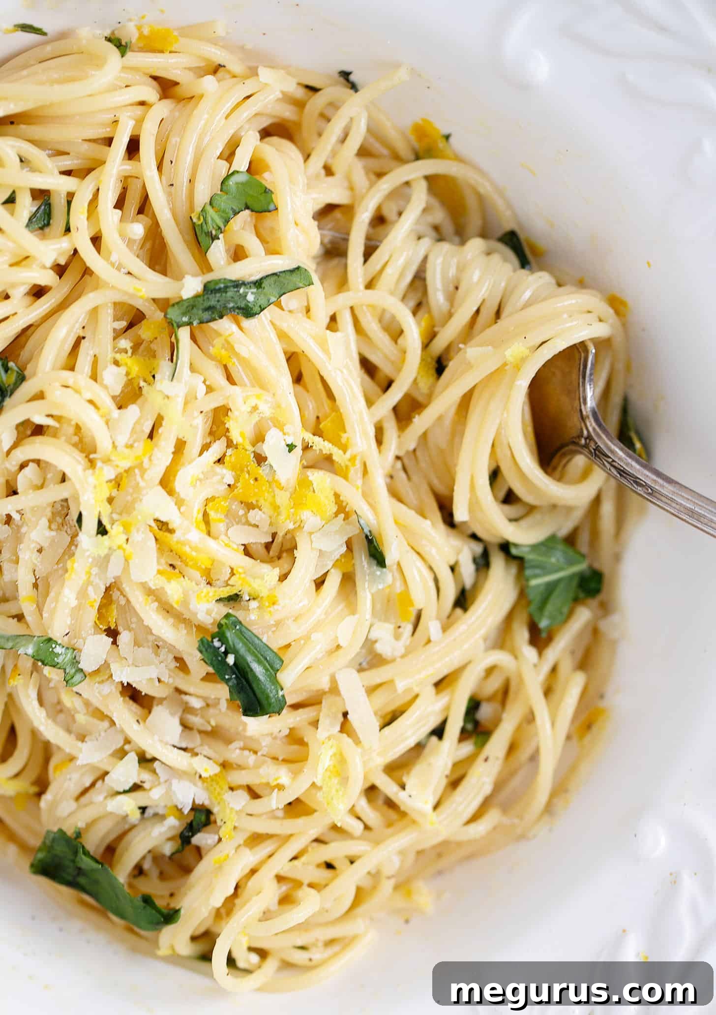 A generously sized portion of creamy lemon pasta, garnished with fresh basil leaves and a lemon wedge, invitingly presented in a white bowl.