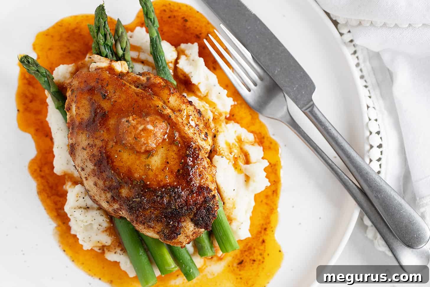 Cajun chicken on plate with mashed potatoes and asparagus, topped with melting honey butter.