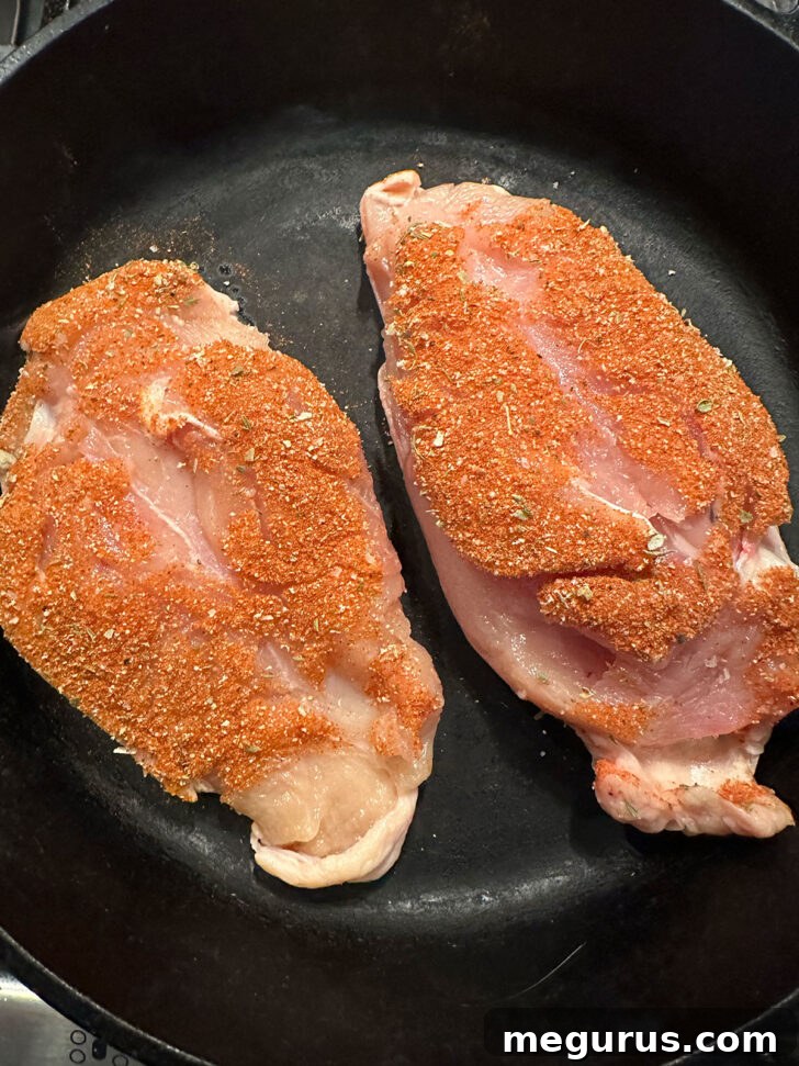 Coated chicken breasts searing in a hot cast iron skillet.