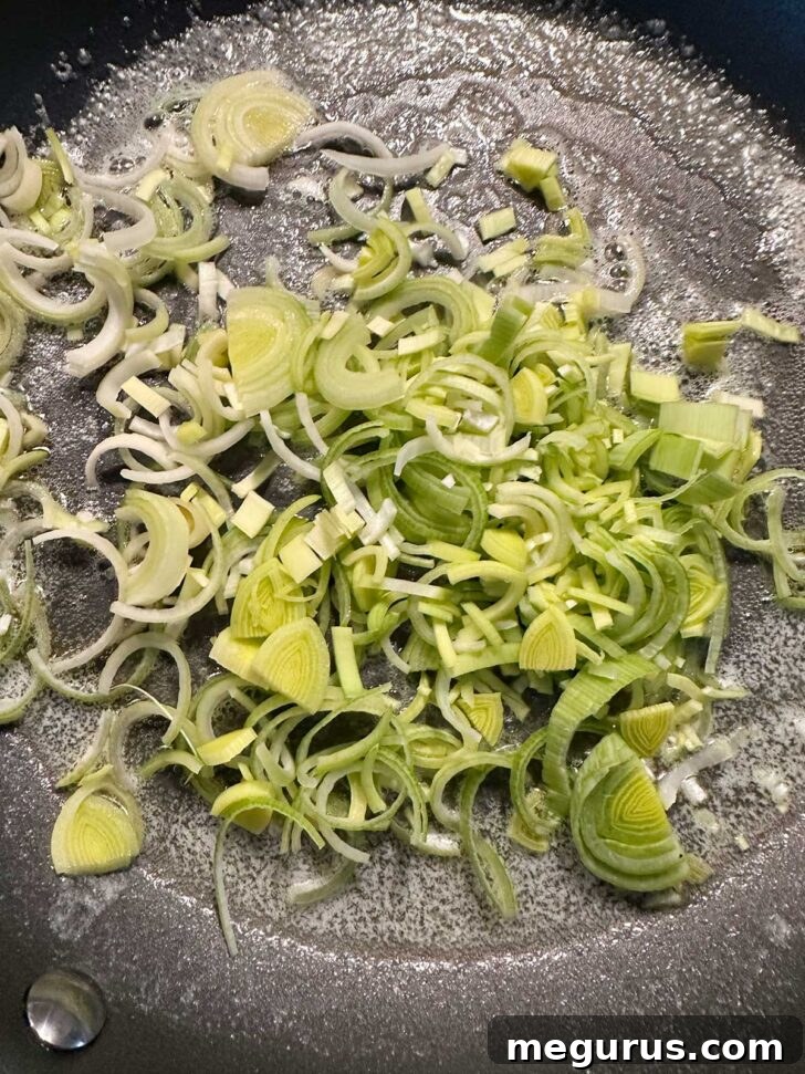 Chopped leeks being added to a hot skillet with melted butter.