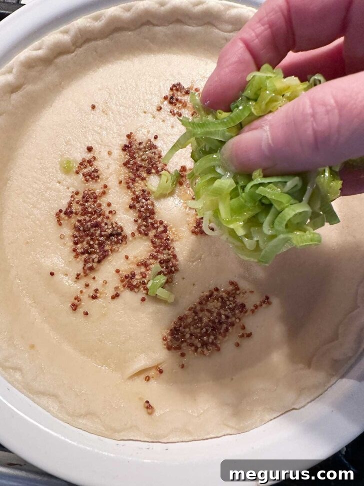 Spreading cooked and cooled leeks evenly over the par-baked pie shell.