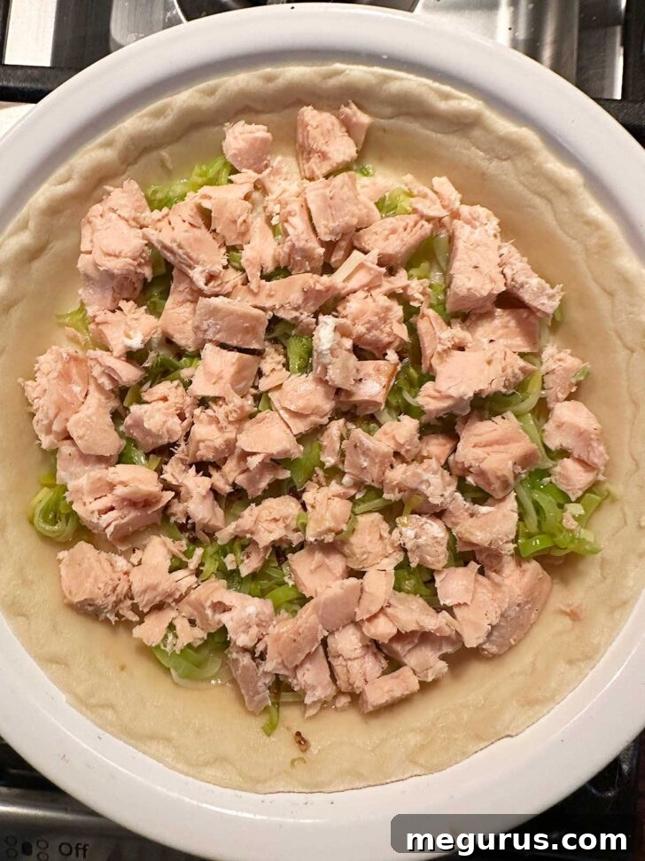 Adding flaked cooked salmon chunks to the pie shell over the leeks.