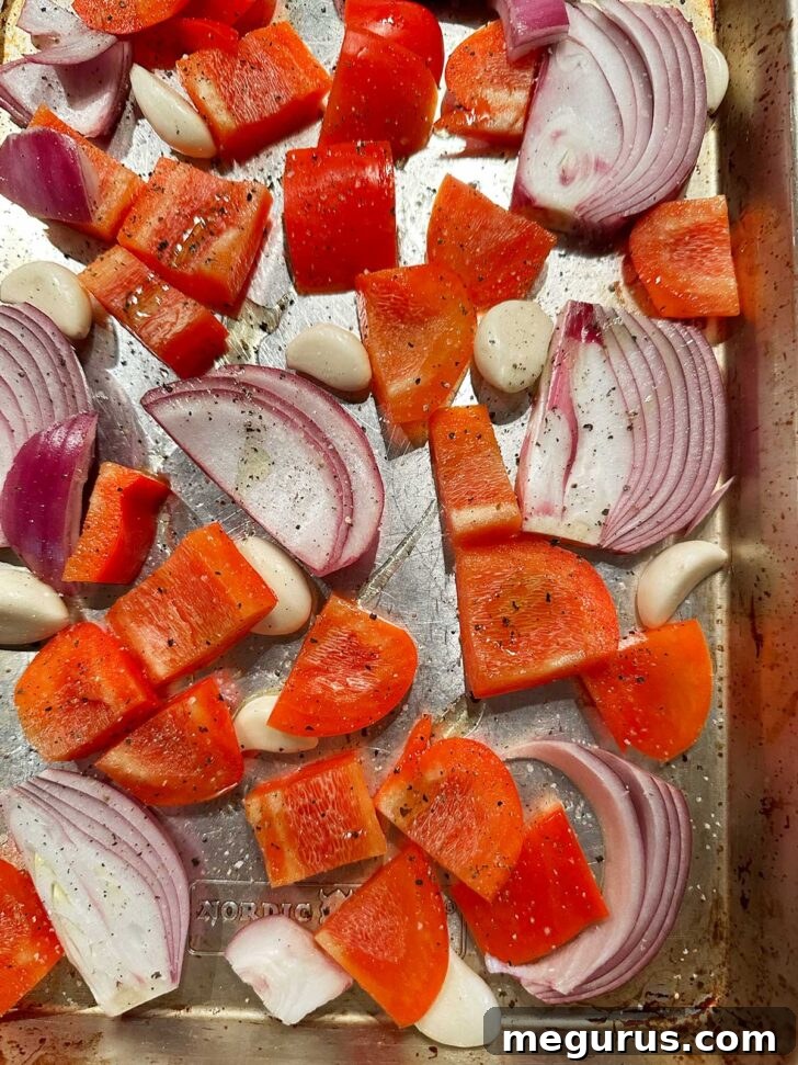 Cut red bell pepper, red onion, and whole garlic cloves on a sheet pan.