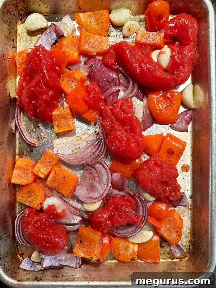 Whole plum tomatoes added to the roasted vegetables on a sheet pan.