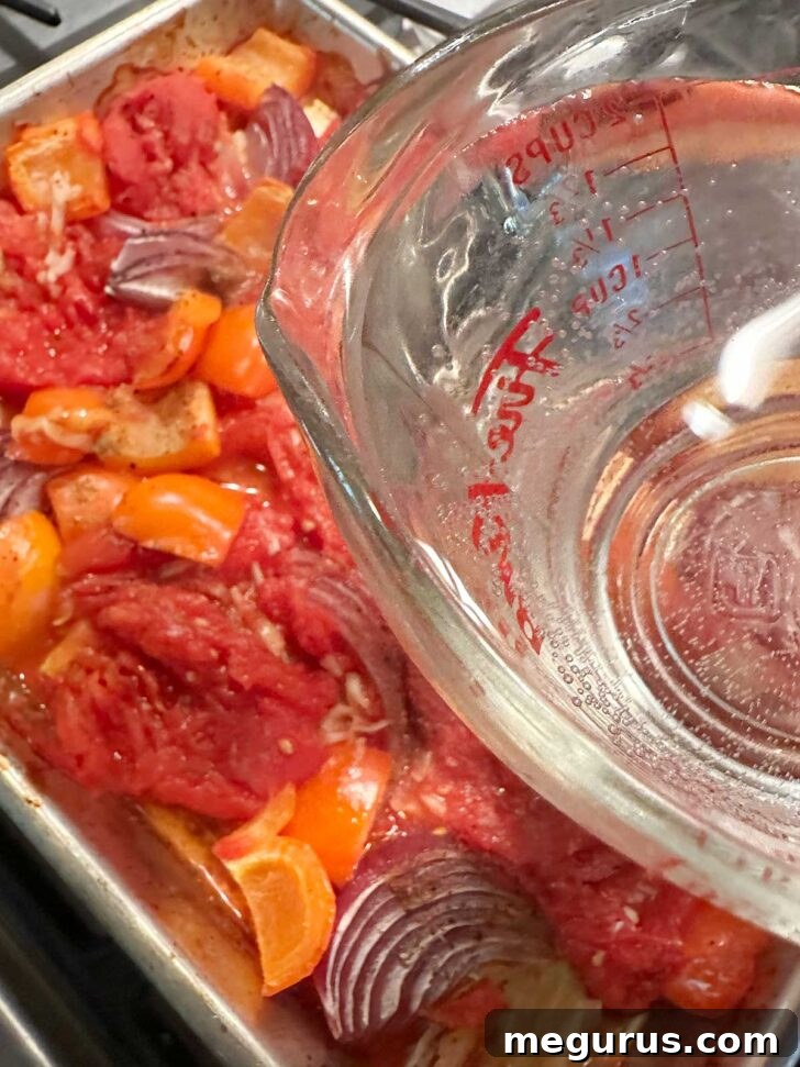 Hot water being poured onto the sheet pan with vegetables and tomatoes.