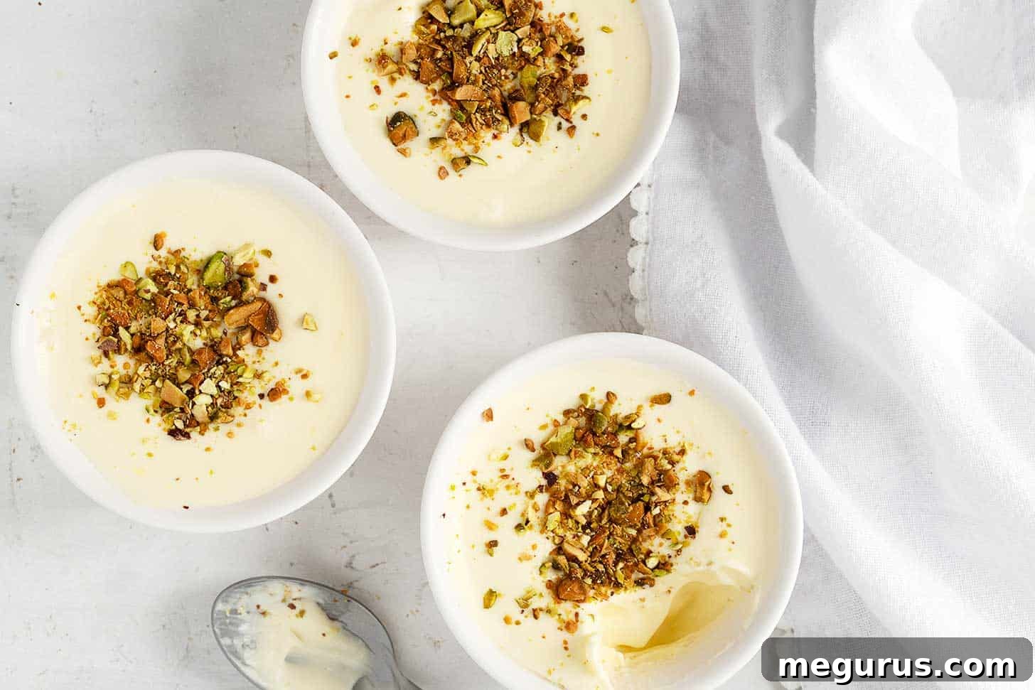 Two ramekins filled with lemon curd pudding, topped with chopped pistachios and a vibrant lemon slice, ready to be served.