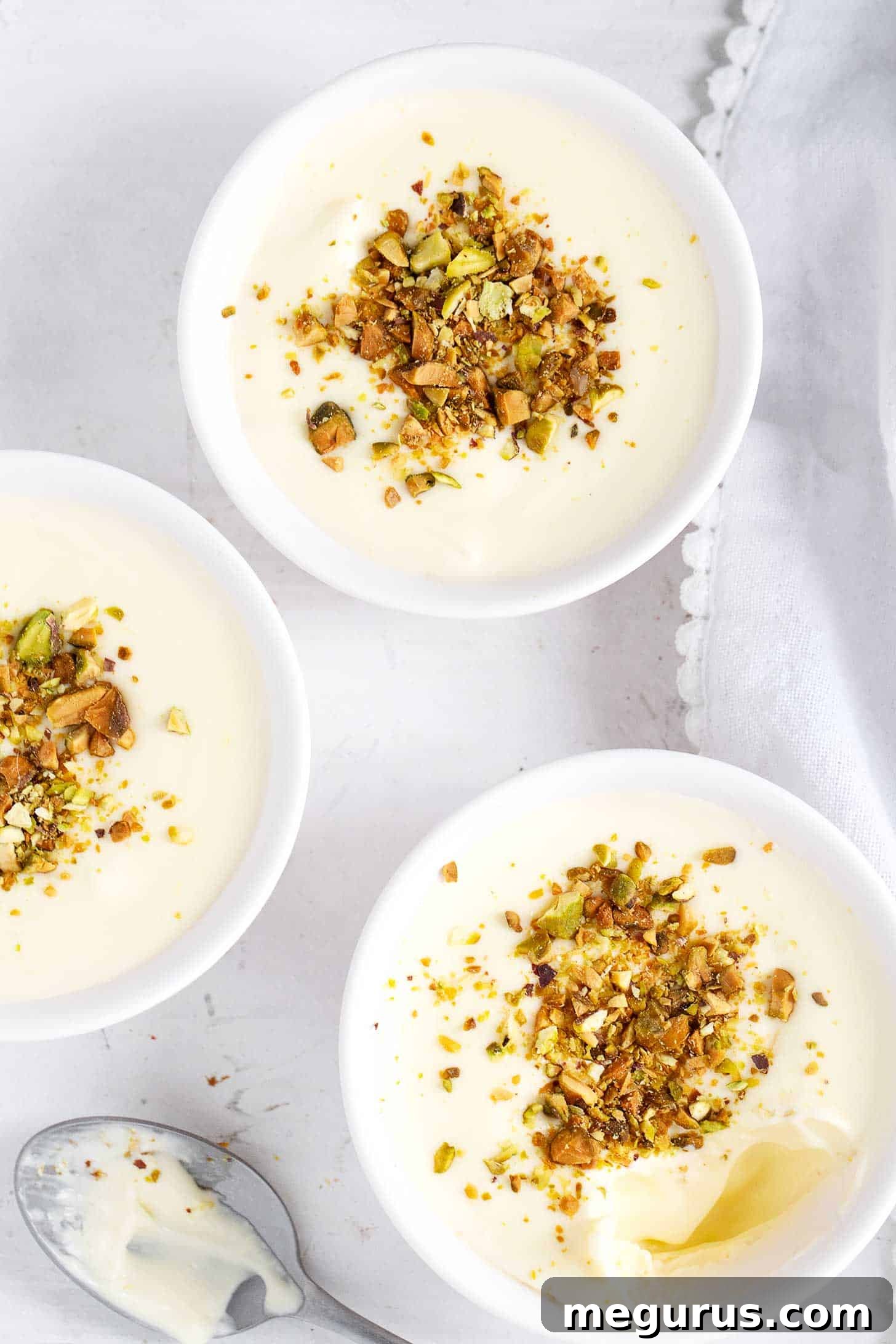 Two artfully arranged lemon curd puddings, adorned with chopped pistachios and fresh lemon slices, sitting on a rustic wooden board.