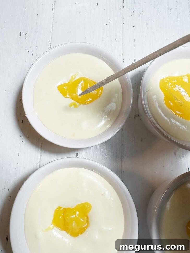 A dollop of lemon curd carefully placed on top of the pudding in a ramekin, with a skewer poised to swirl it in.