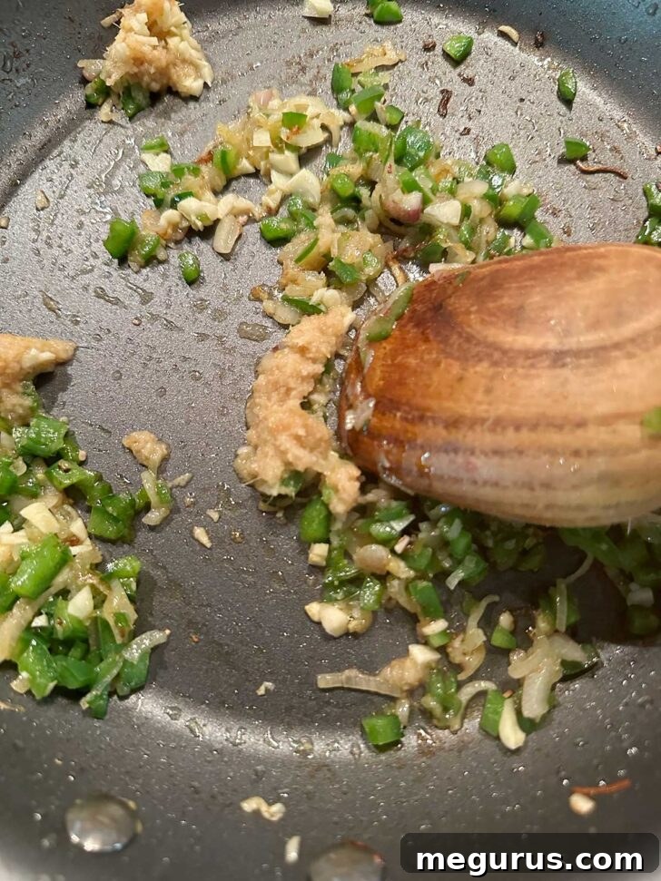 Adding minced garlic and ginger to the simmering shallots and jalapeño in the skillet.