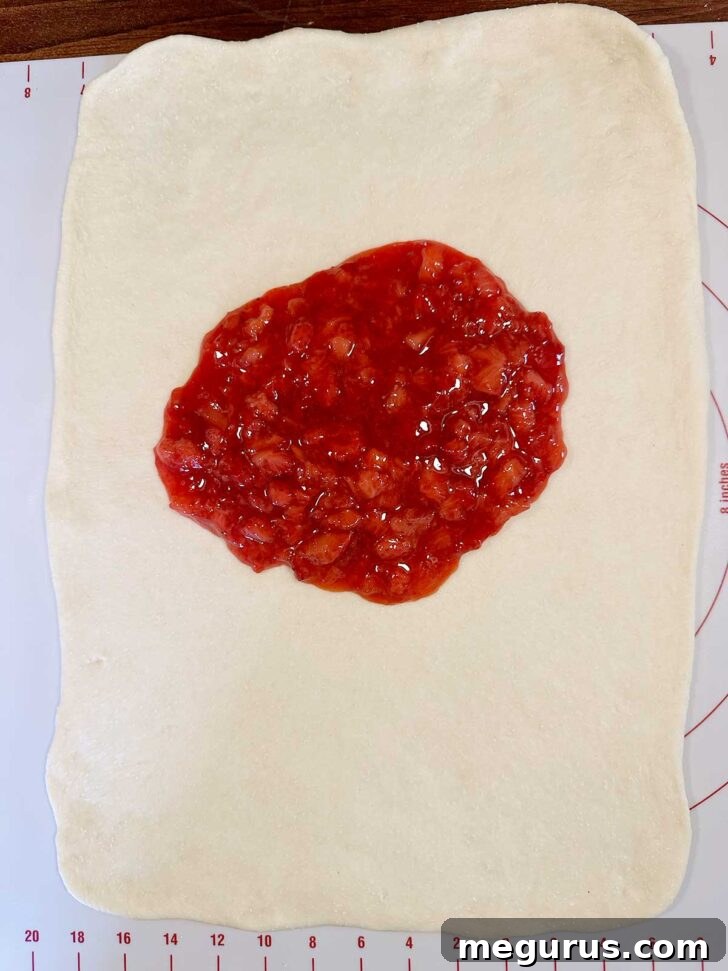 Strawberries spooned on top of dough rectangle.