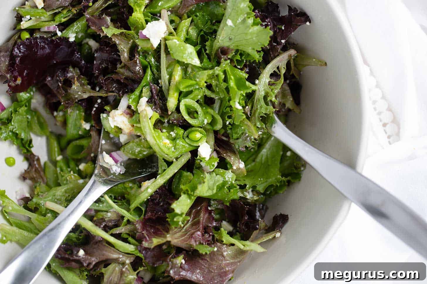 Chopped Spring salad with asparagus and snap peas in bowl. A close-up shot of a refreshing spring salad with green asparagus, snap peas, red onion, and crumbled feta cheese, dressed in a bright vinaigrette.