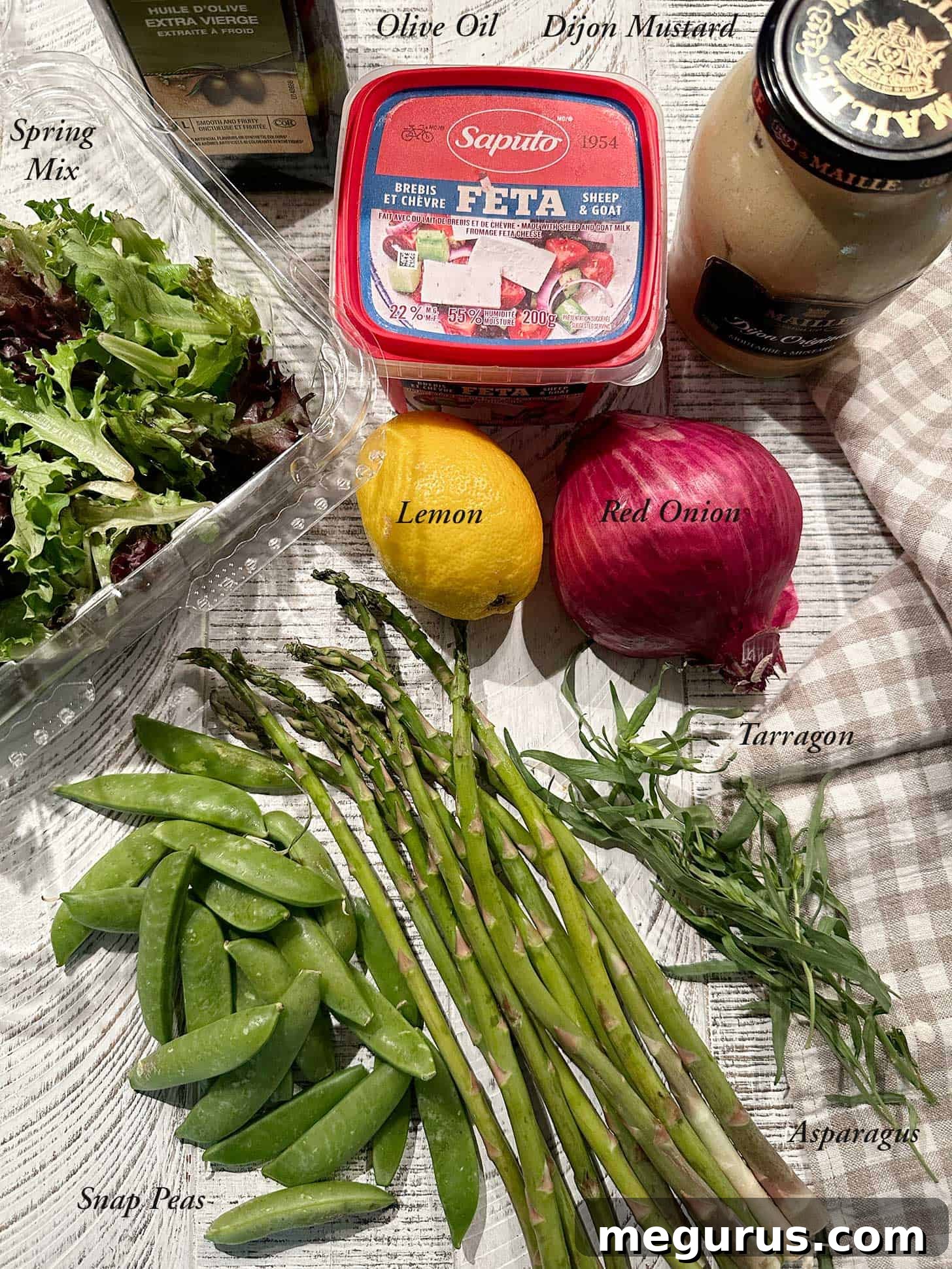 Ingredients for a simple Spring salad. A flat lay of fresh salad ingredients including Spring mix lettuce, asparagus, snap peas, red onion, feta cheese, lemon, tarragon, olive oil, and Dijon mustard.