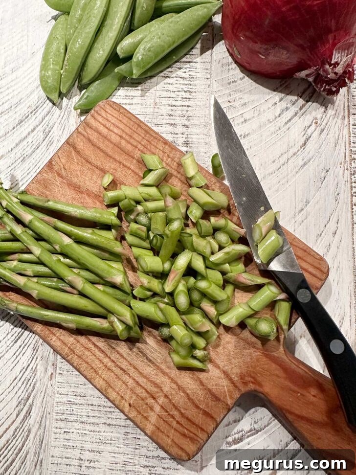 Asparagus being chopped on a cutting board. Thin green asparagus spears are being diagonally chopped into small pieces on a wooden cutting board.
