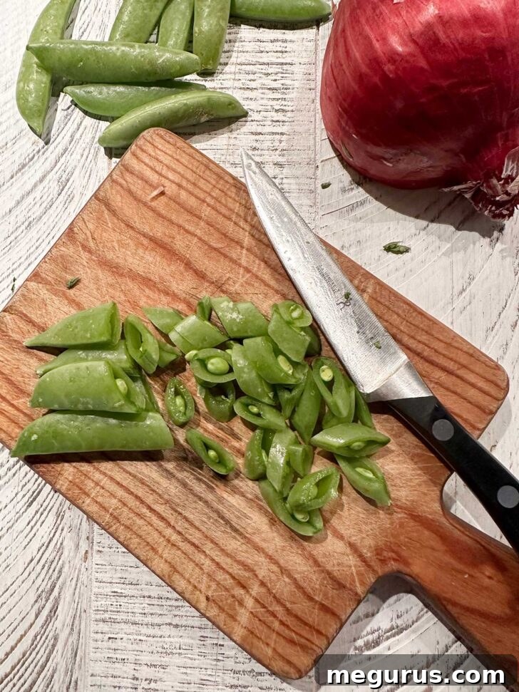 Snap peas being chopped on a cutting board. Fresh green snap peas are being diagonally sliced into small pieces on a wooden cutting board.