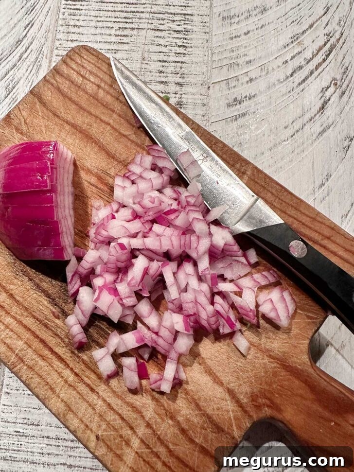 Red onion being chopped on a cutting board. A red onion is being finely diced on a wooden cutting board with a knife.