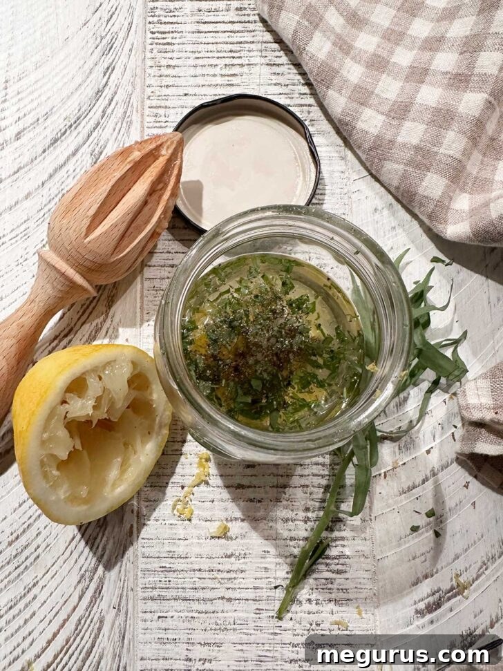 Lemon tarragon vinaigrette ingredients in a small jar. A small glass jar contains olive oil, lemon zest, tarragon, Dijon mustard, and honey, ready to be shaken into a vinaigrette.