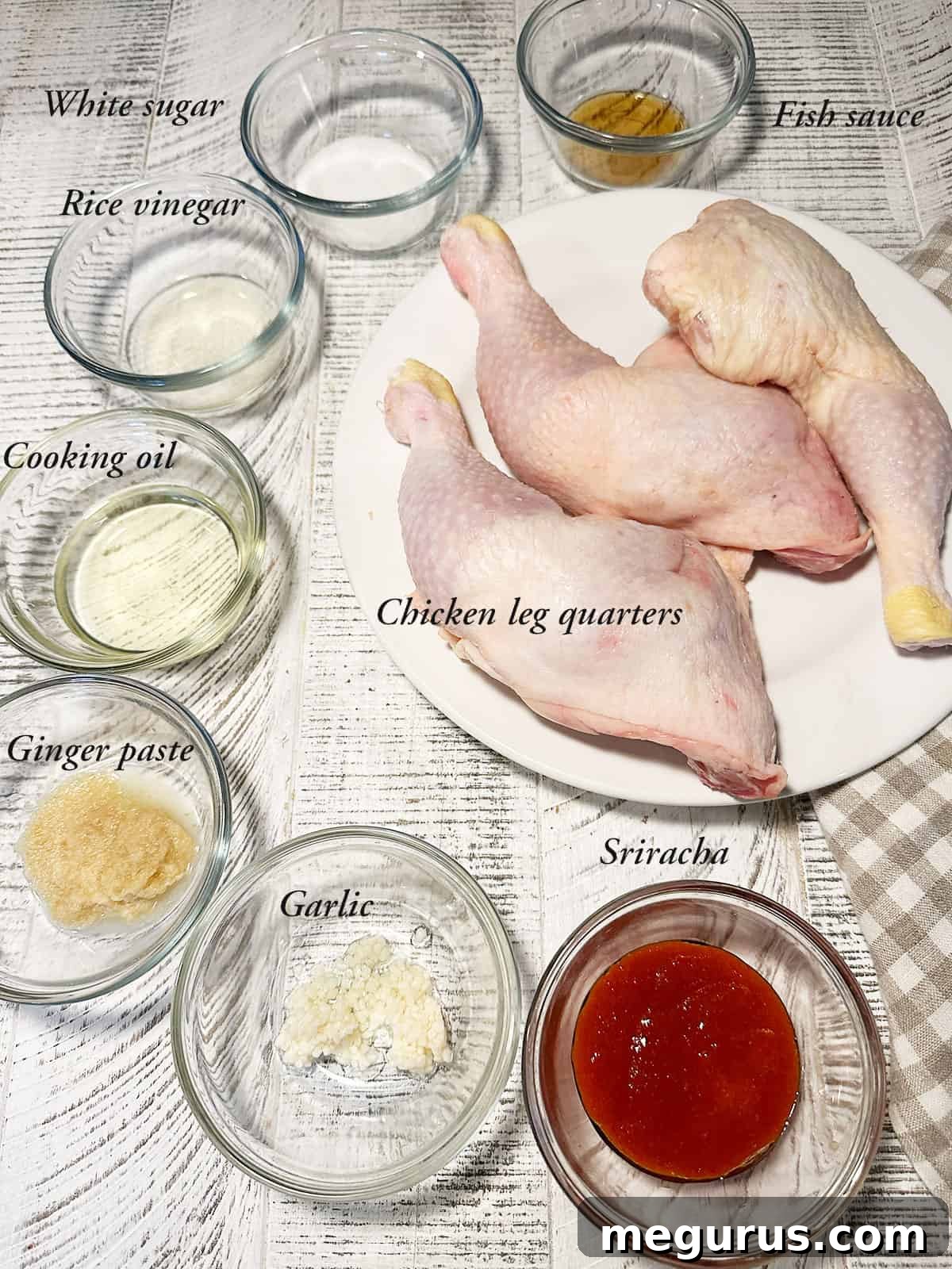 Assortment of fresh ingredients for Sriracha oven chicken legs including chicken leg quarters, Sriracha sauce, fresh ginger, minced garlic, and rice vinegar in small bowls.