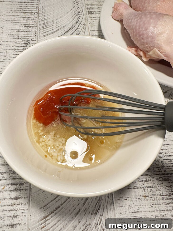 Ingredients for the Sriracha basting sauce being whisked together in a small bowl, showcasing its smooth consistency.