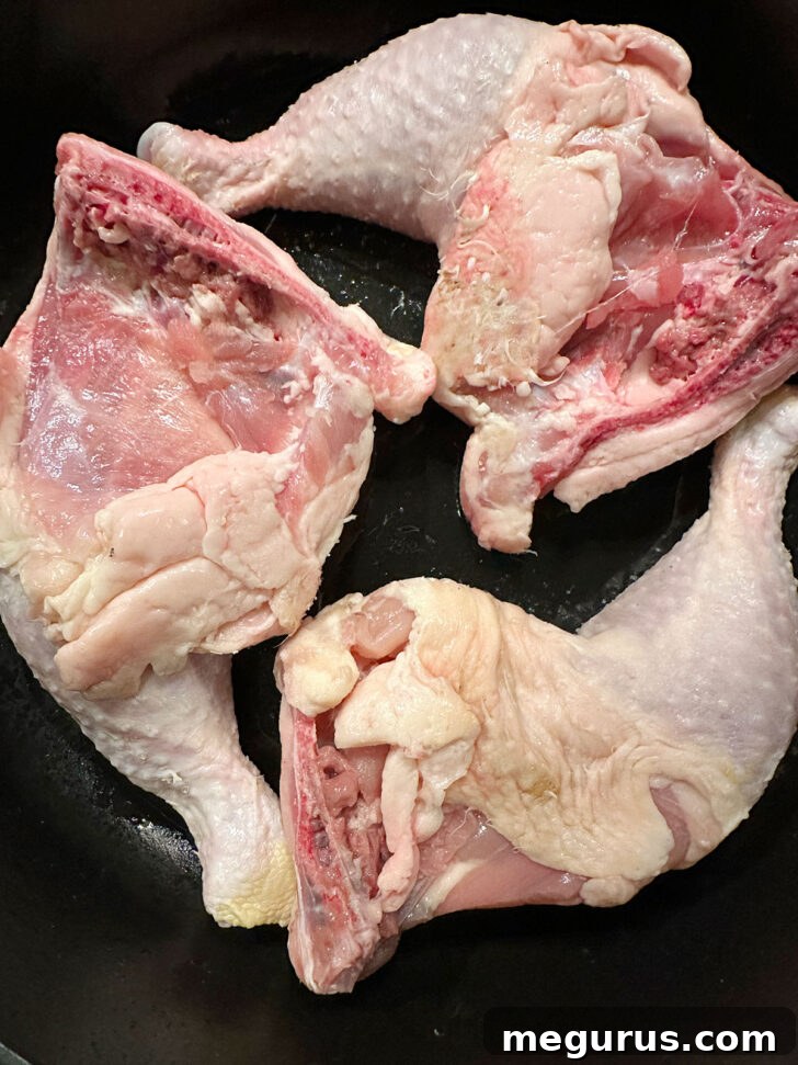 Chicken legs with seasoned skin side down in a hot skillet, beginning to crisp and brown.