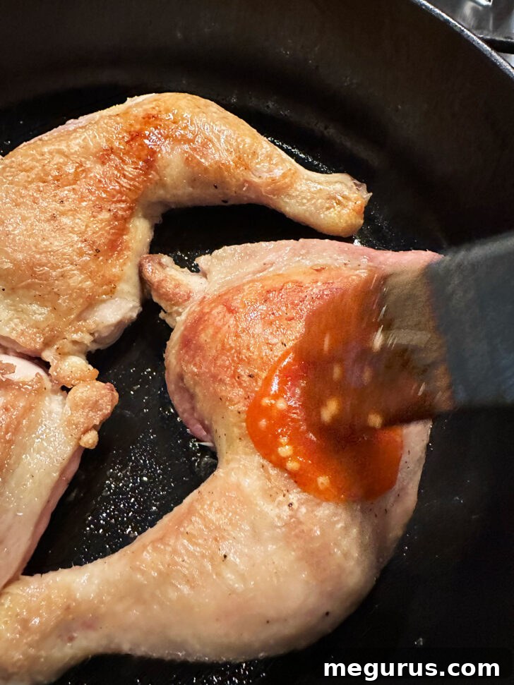 Chef basting the flipped chicken legs generously with Sriracha sauce using a silicone brush before transferring to the oven.