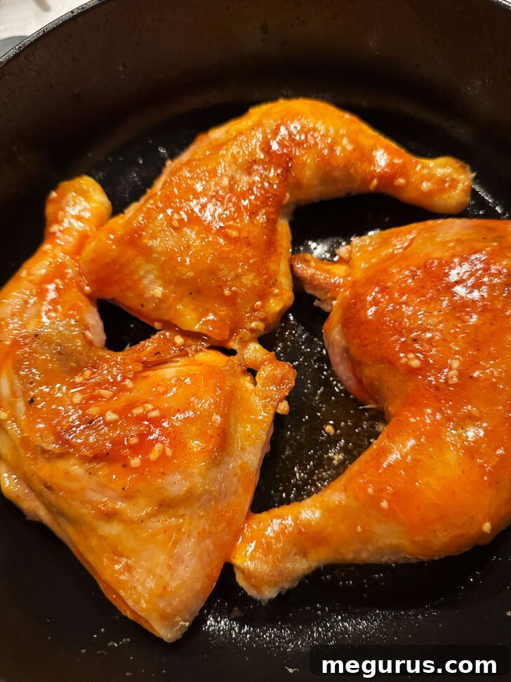 Oven-baked Sriracha chicken legs, glistening with a rich sauce, resting in the skillet after cooking, ready for garnishing.