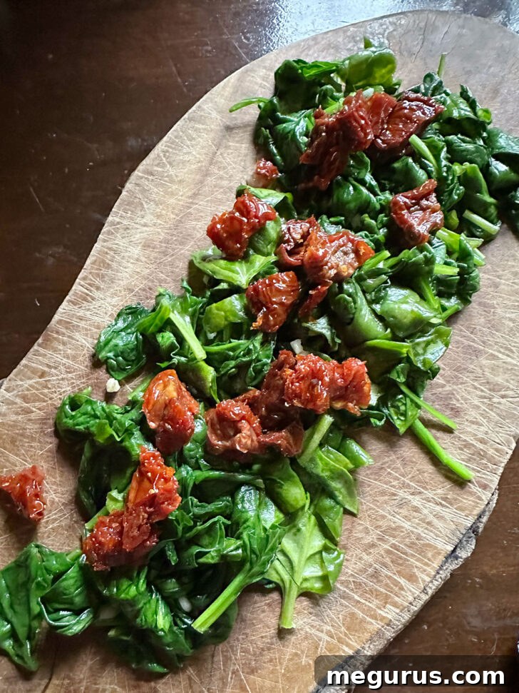 Wilted spinach chopped on cutting board with sun-dried tomatoes.