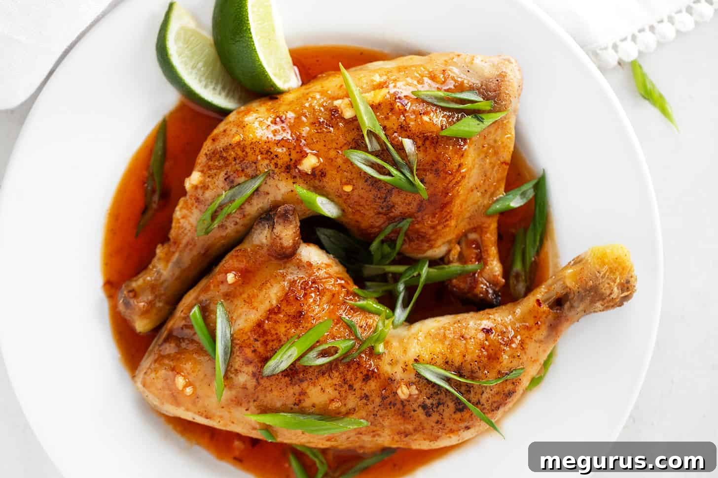 Crispy hot honey chicken legs on a plate, garnished with fresh green onions and lime wedges.