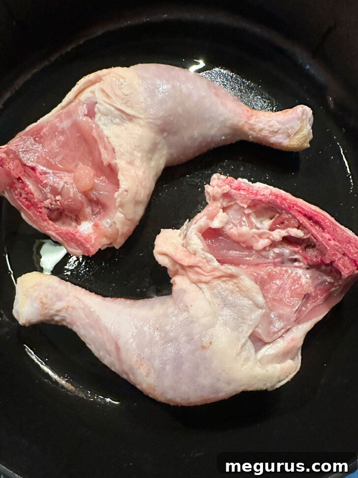 Chicken legs sizzling in a hot skillet, skin side down.