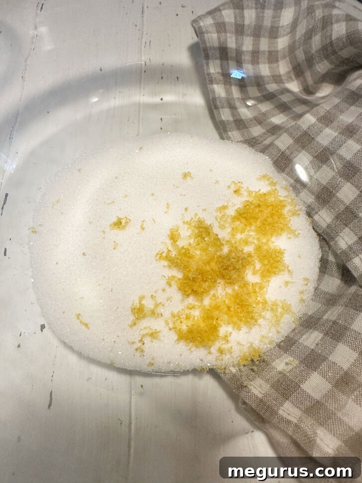 Lemon zest being rubbed into granulated sugar in a mixing bowl.