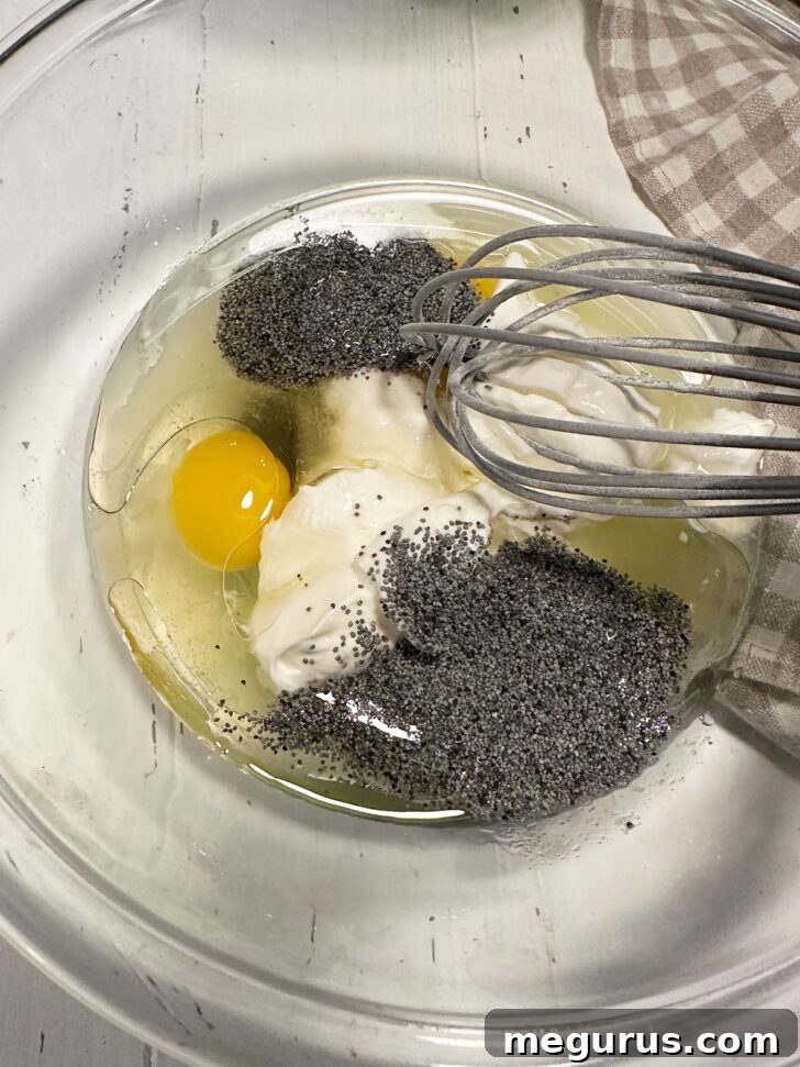 Wet ingredients, including oil, eggs, vanilla, sour cream, and poppy seeds, whisked in a separate bowl.