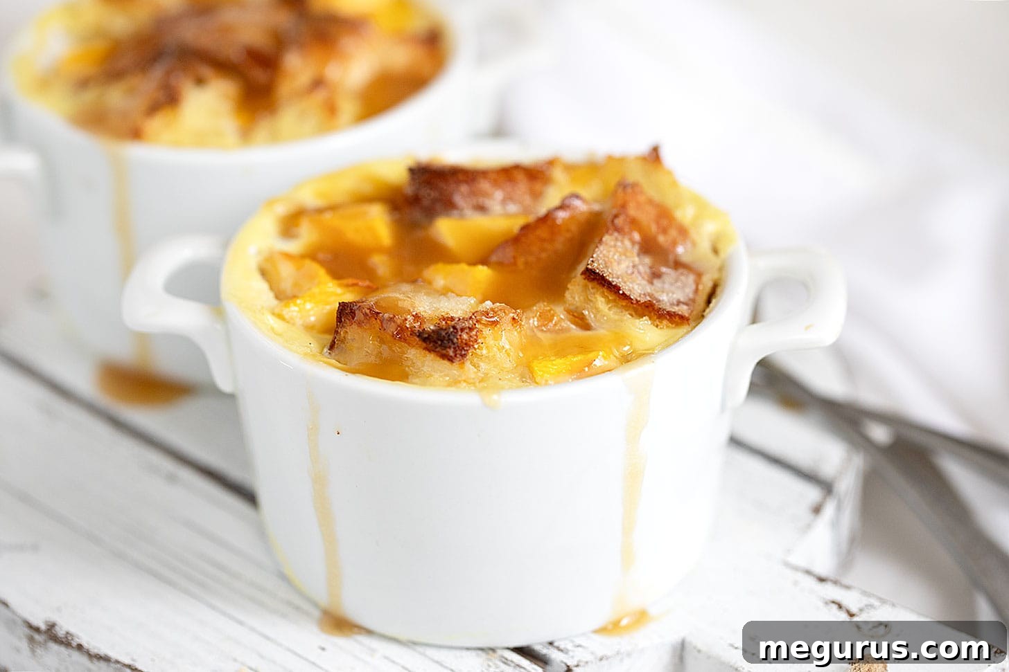Golden-brown peach bread pudding in ramekins, drizzled with warm brown sugar sauce