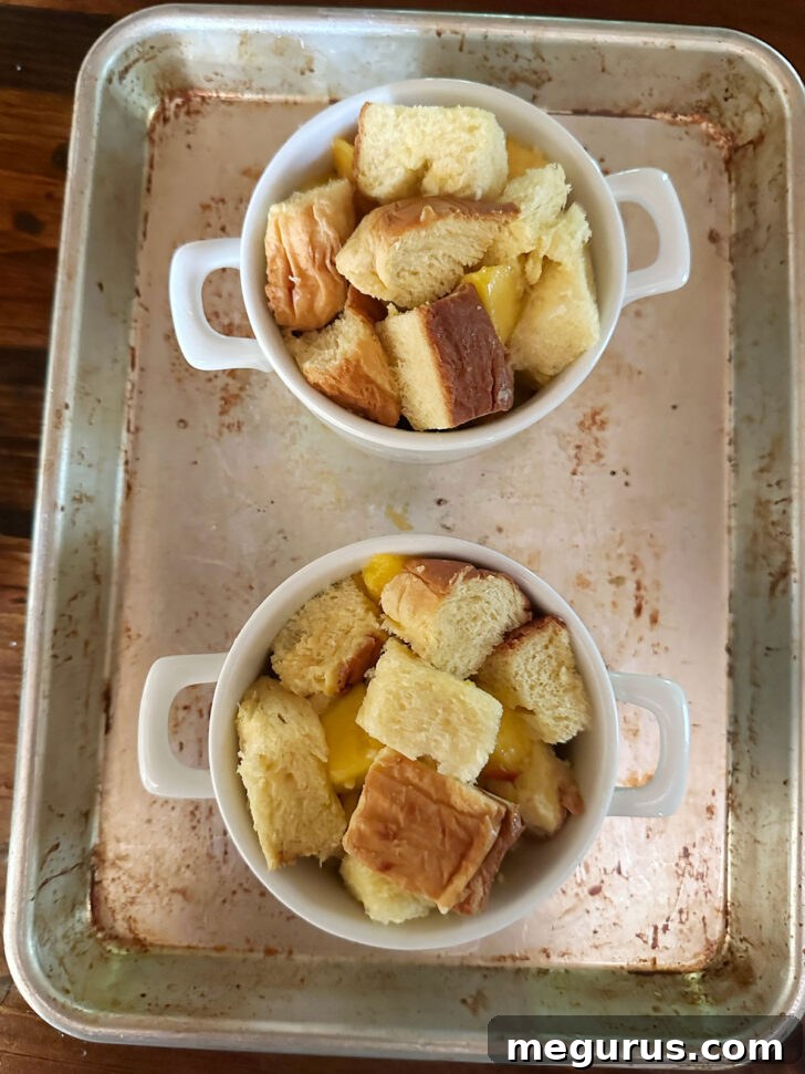 Bread cubes and chopped peaches neatly arranged in individual ramekins on a baking sheet