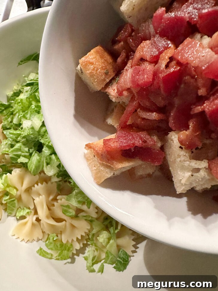 Crispy cooked bacon bits and golden homemade croutons being added to the salad bowl with pasta and romaine, building layers of flavor.