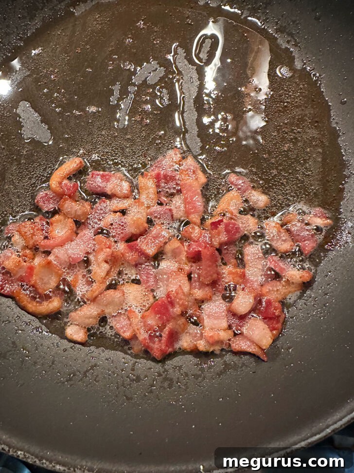 Crispy diced bacon in a hot skillet, freshly cooked and ready to be removed, leaving behind flavorful bacon fat.