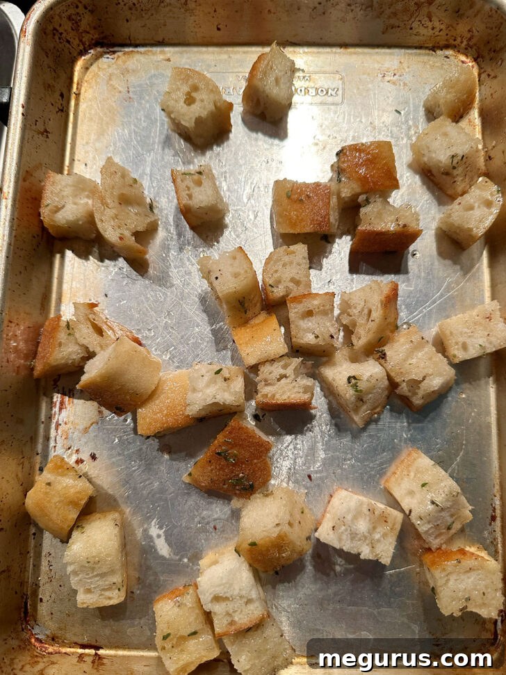 Seasoned bread cubes evenly scattered on a baking sheet, ready for the oven to transform them into golden, crispy croutons.
