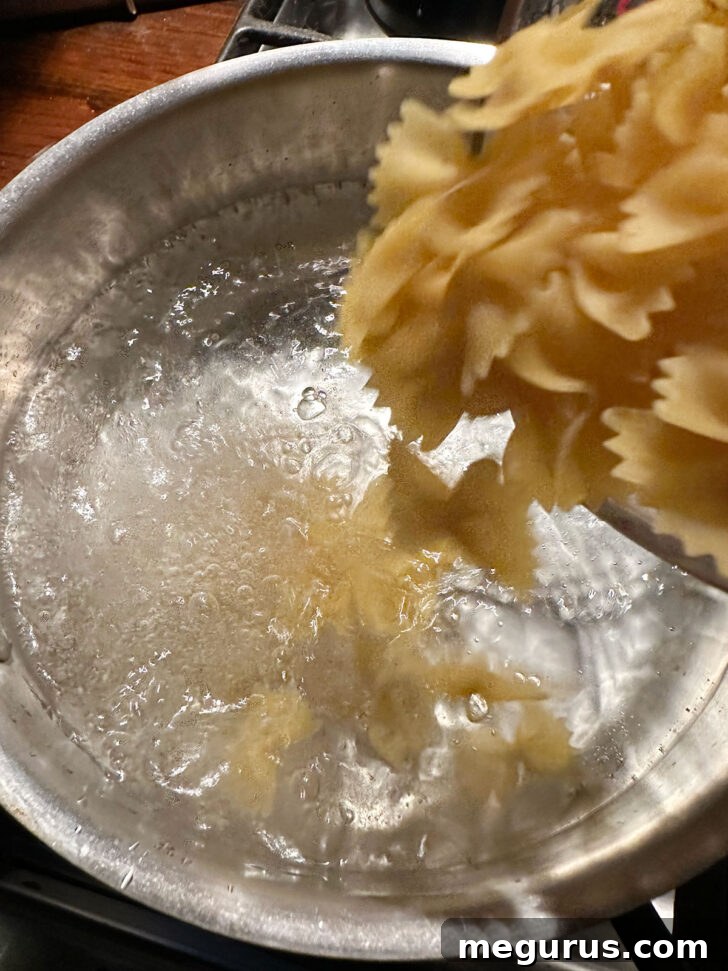 Bowtie pasta being added to a large pot of vigorously boiling, salted water, ensuring proper cooking for an al dente finish.